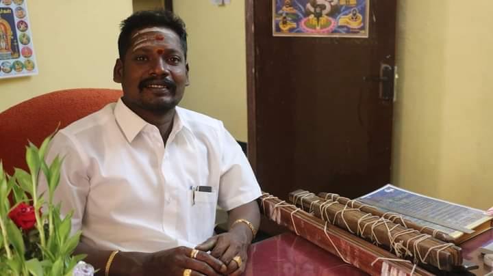 Guruji B.S. Vignesh Swamy seated at his desk with a bundle of palm-leaf manuscripts